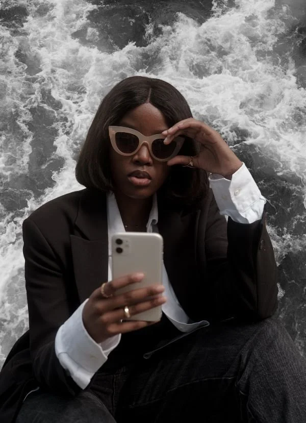 PLEB Group SEO woman in a black suit looking at her phone wearing sunglasses with water in the background