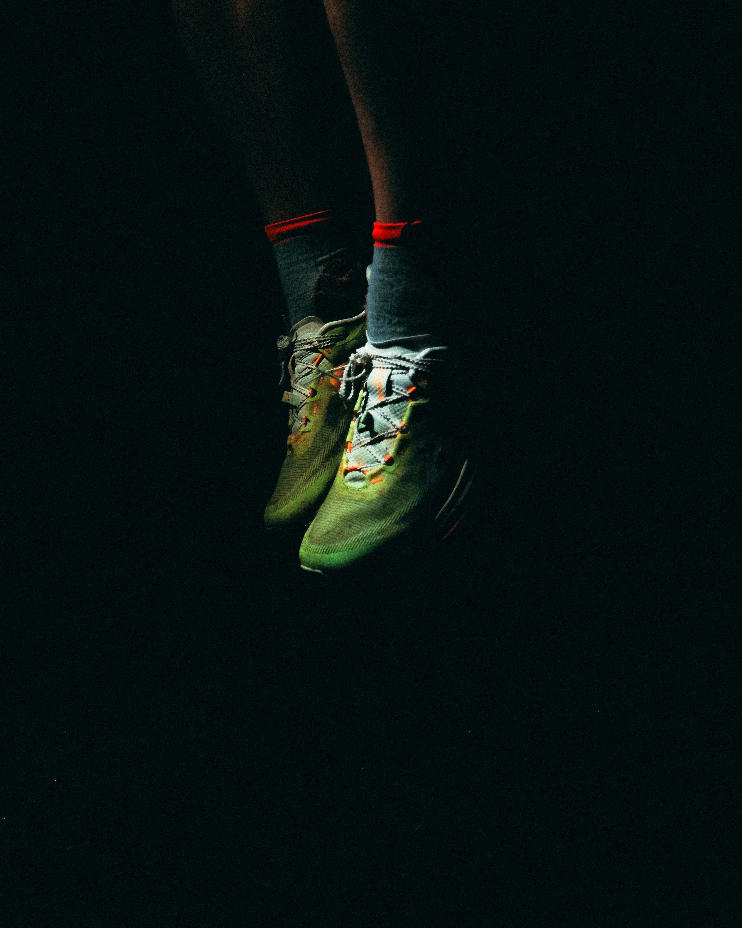 Chaussures de course jaune avec chaussettes grises, vue du dessous, dans un environnement sombre.