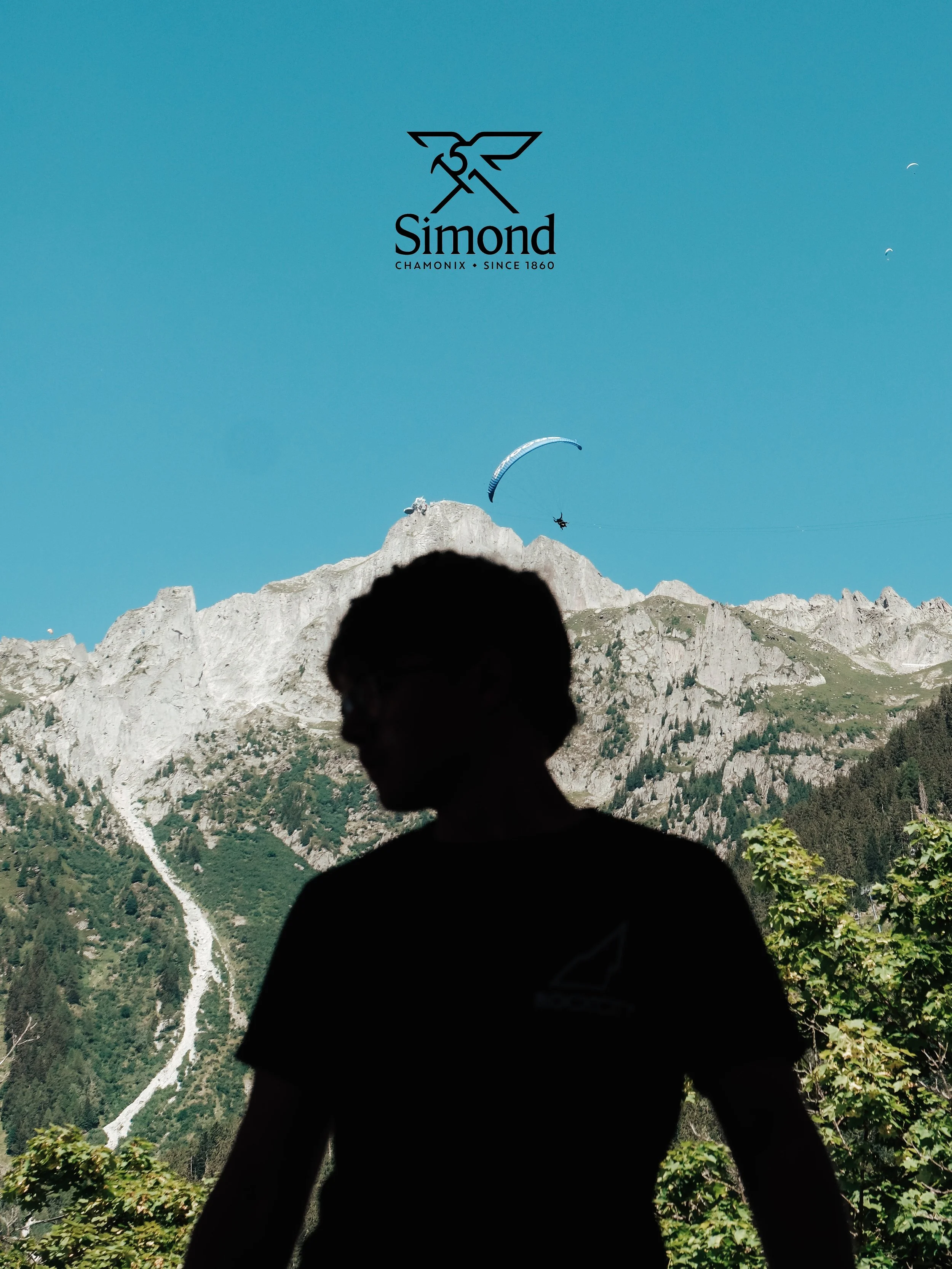 Silhouette d'un enfant devant un paysage montagneux avec un cerf-volant dans le ciel et un logo Simond en haut au centre, fond bleu clair.