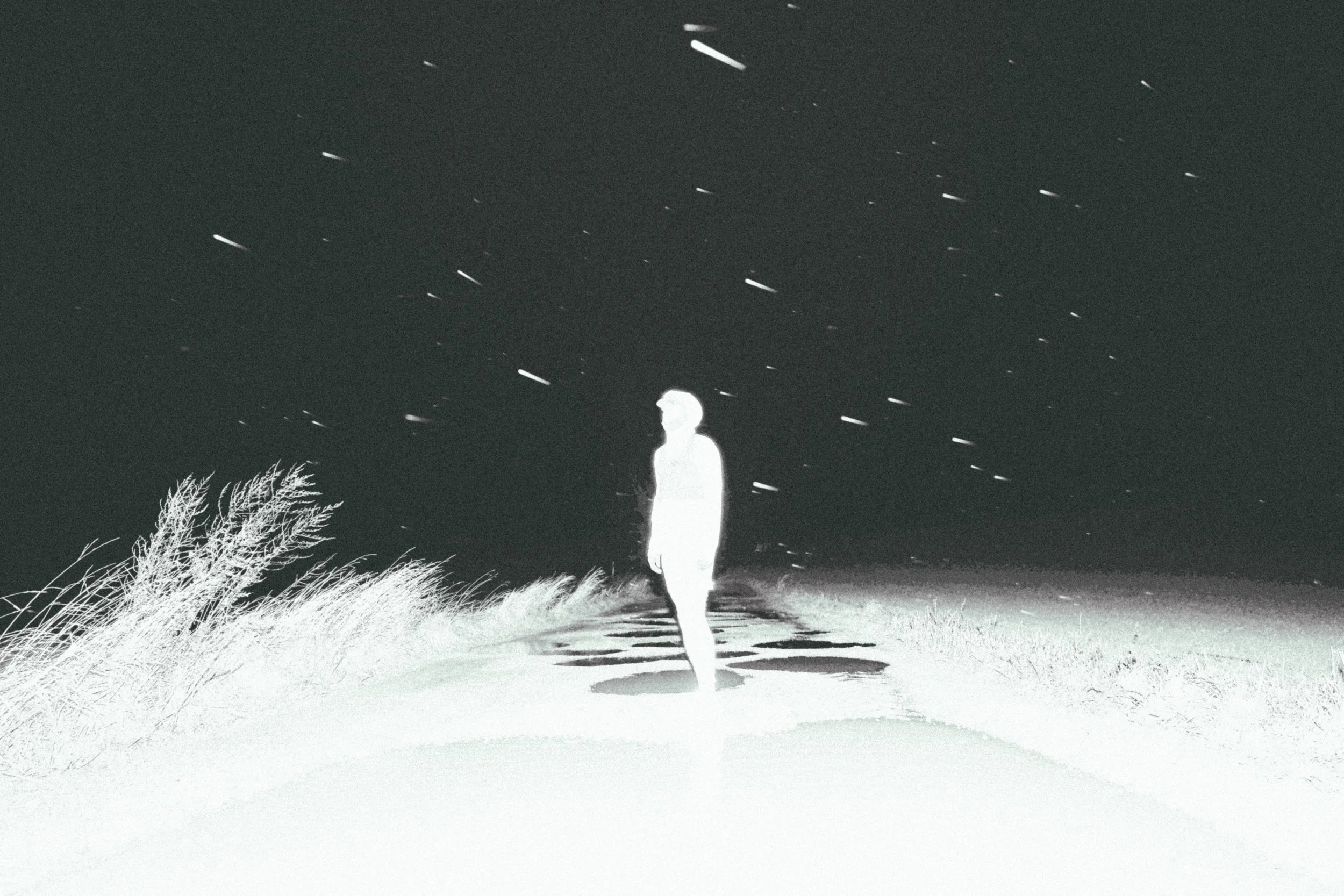 Une silhouette blanche d'une personne marchant sur une plage pendant la nuit, avec un ciel étoilé et des nuages qui passent rapidement.