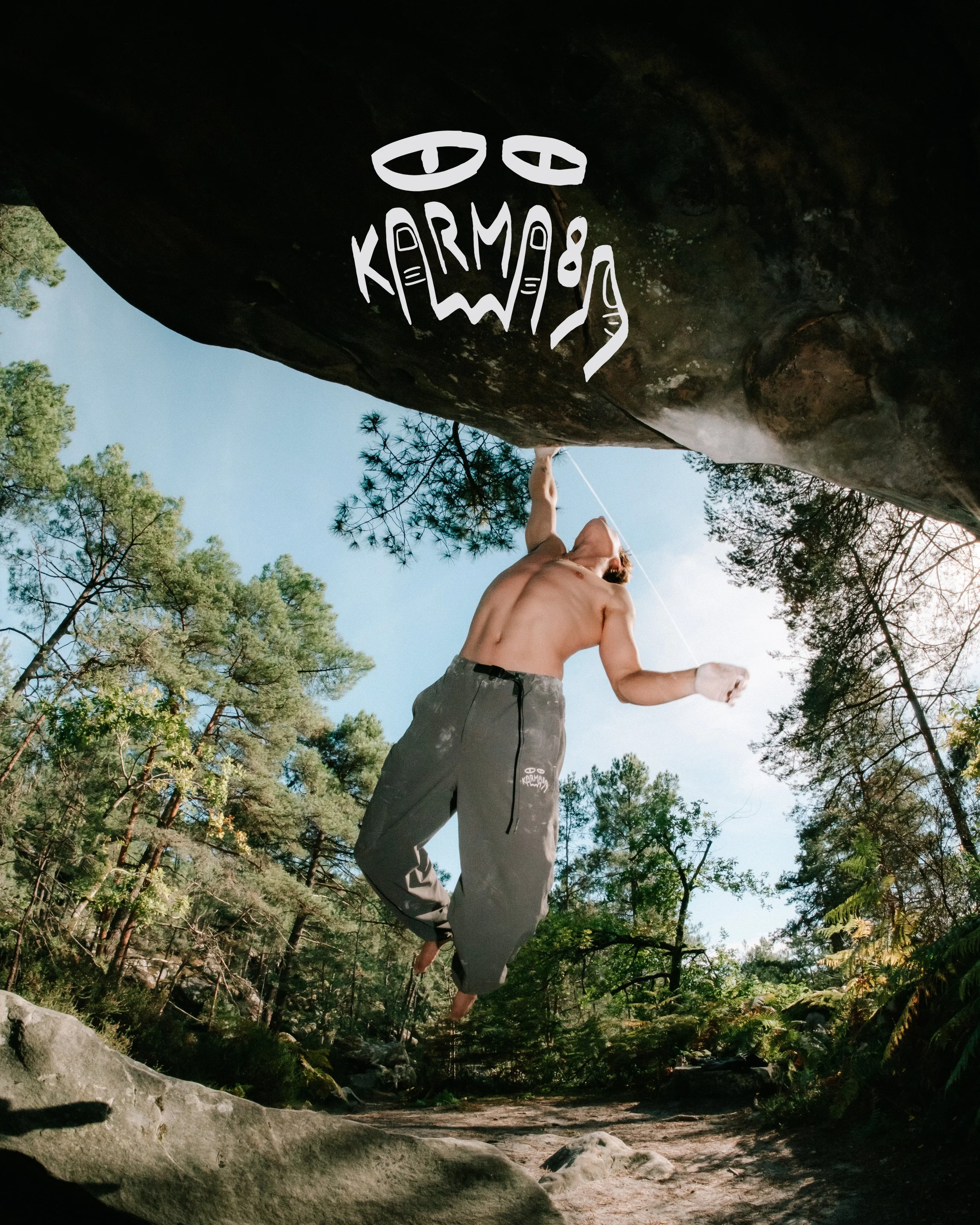 Une personne en short et sans haut, avec un chapeau, en position de planche ou de yoga, est appuyée contre une grande roche dans une forêt avec arbres et ciel bleu.