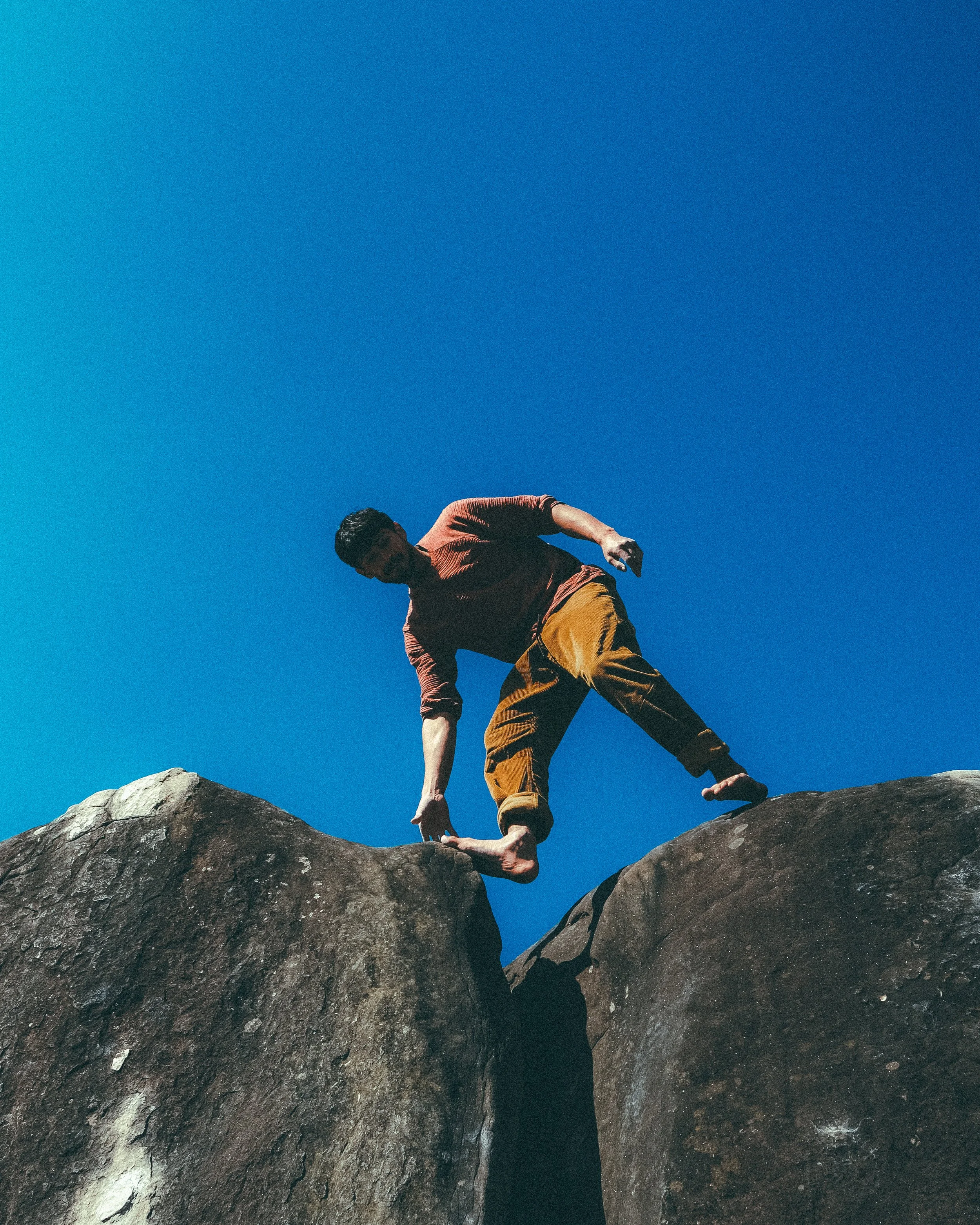 Une personne en tenue de randonnée grimpe sur des rochers en plein air, avec un ciel bleu clair en arrière-plan.