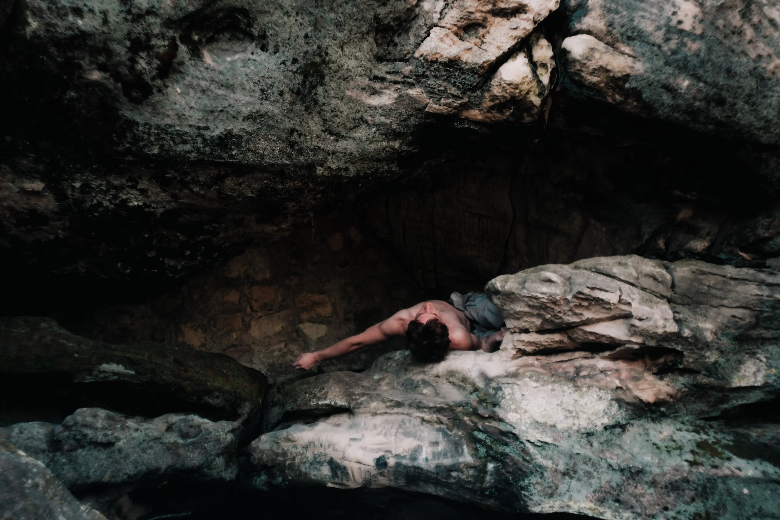 Personne allongée dans une cavité rocheuse entre des rochers.