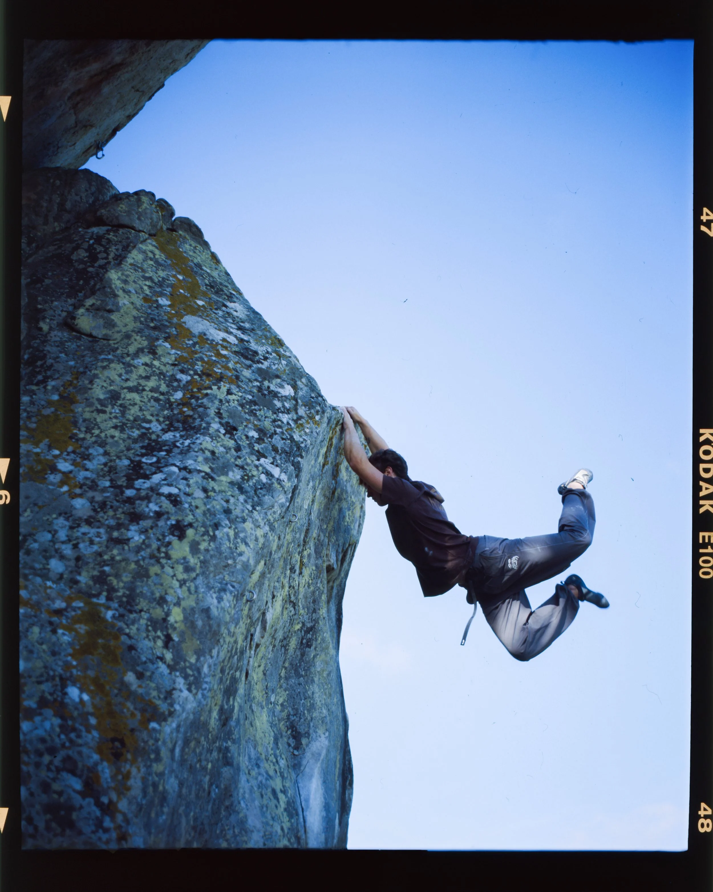 Photo d'un homme en train d'escalader une falaise rocheuse en utilisant une technique de grimpe, avec un ciel clair en arrière-plan.