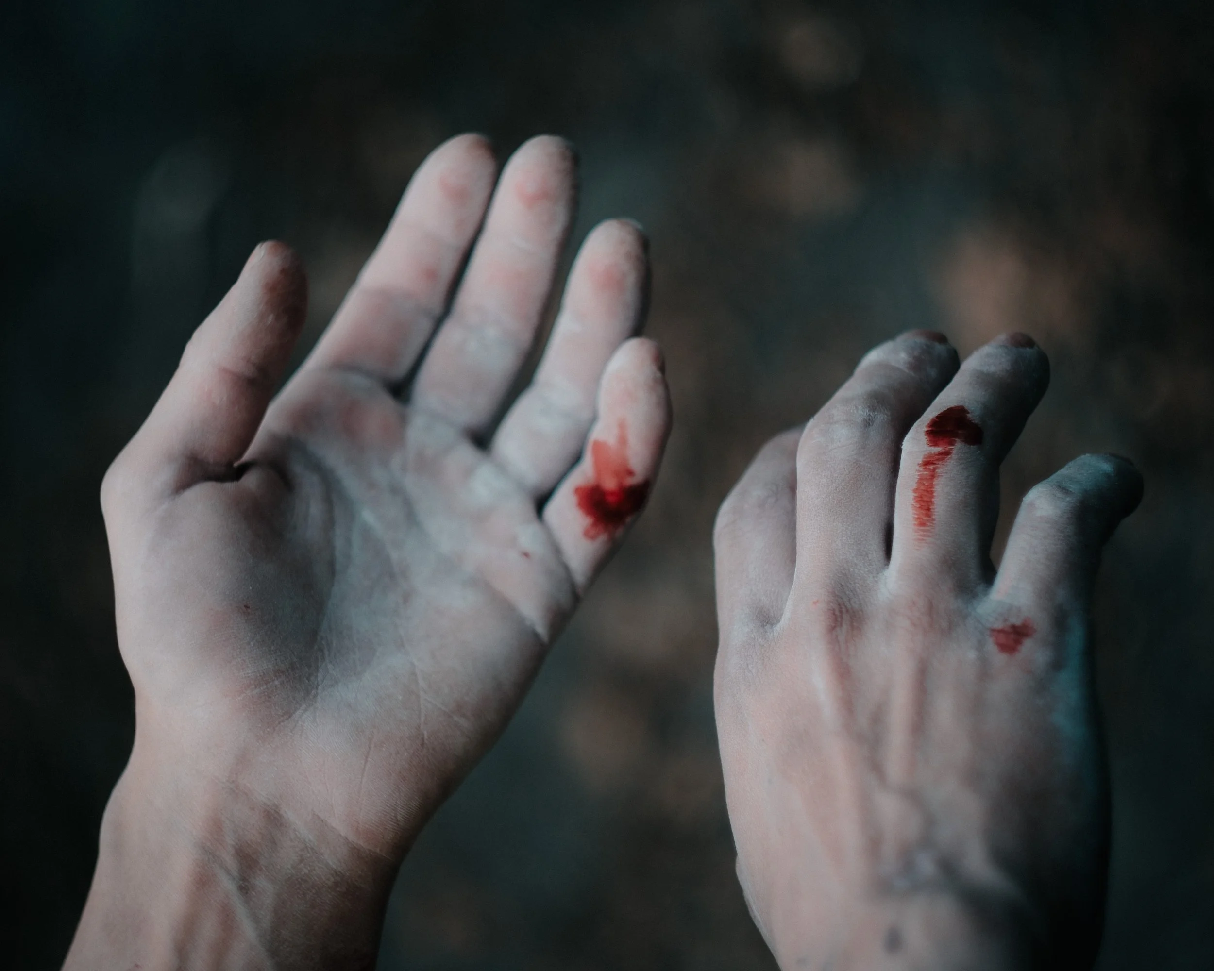 Mains couvertes de poussière ou de craie, avec quelques traces de sang, caressant une surface sombre et floue.