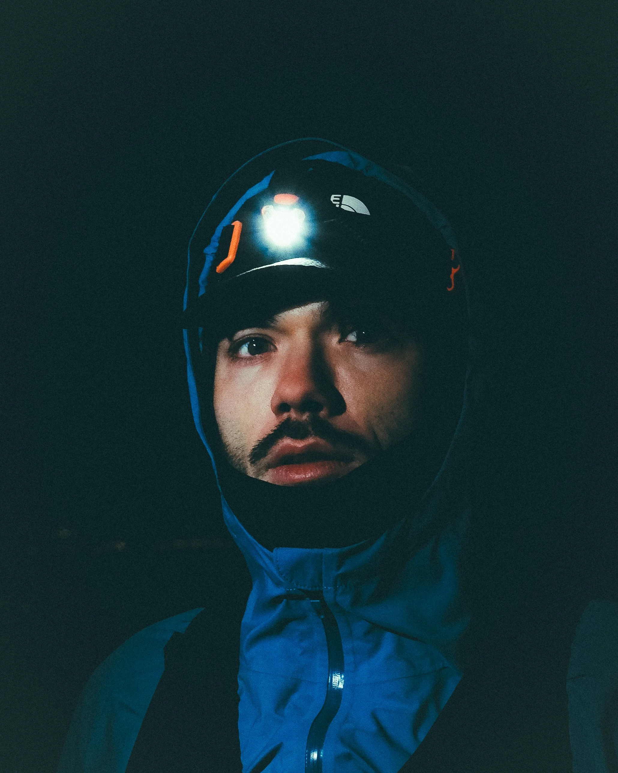 Premier plan d'un homme portant un casque de vélo avec lumière intégrée, portant une veste bleu foncé, dans l'obscurité.