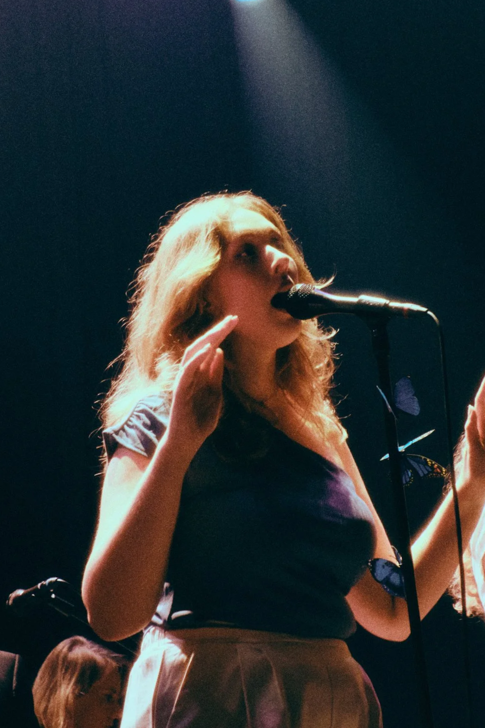 Vrouw zingt in een microfoon op een donkere achtergrond, met zachte verlichting.