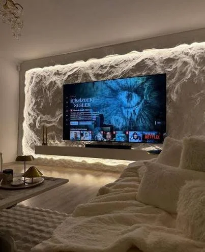 Living room with a TV mounted on a textured wall, featuring a large feline face display, and a cream-colored couch with a cozy blanket.