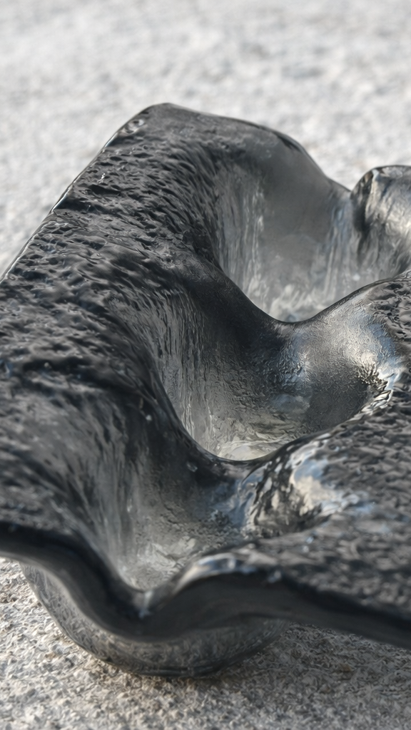 Un oggetto di vetro nero con forma ondulata, posato su una superficie grigia