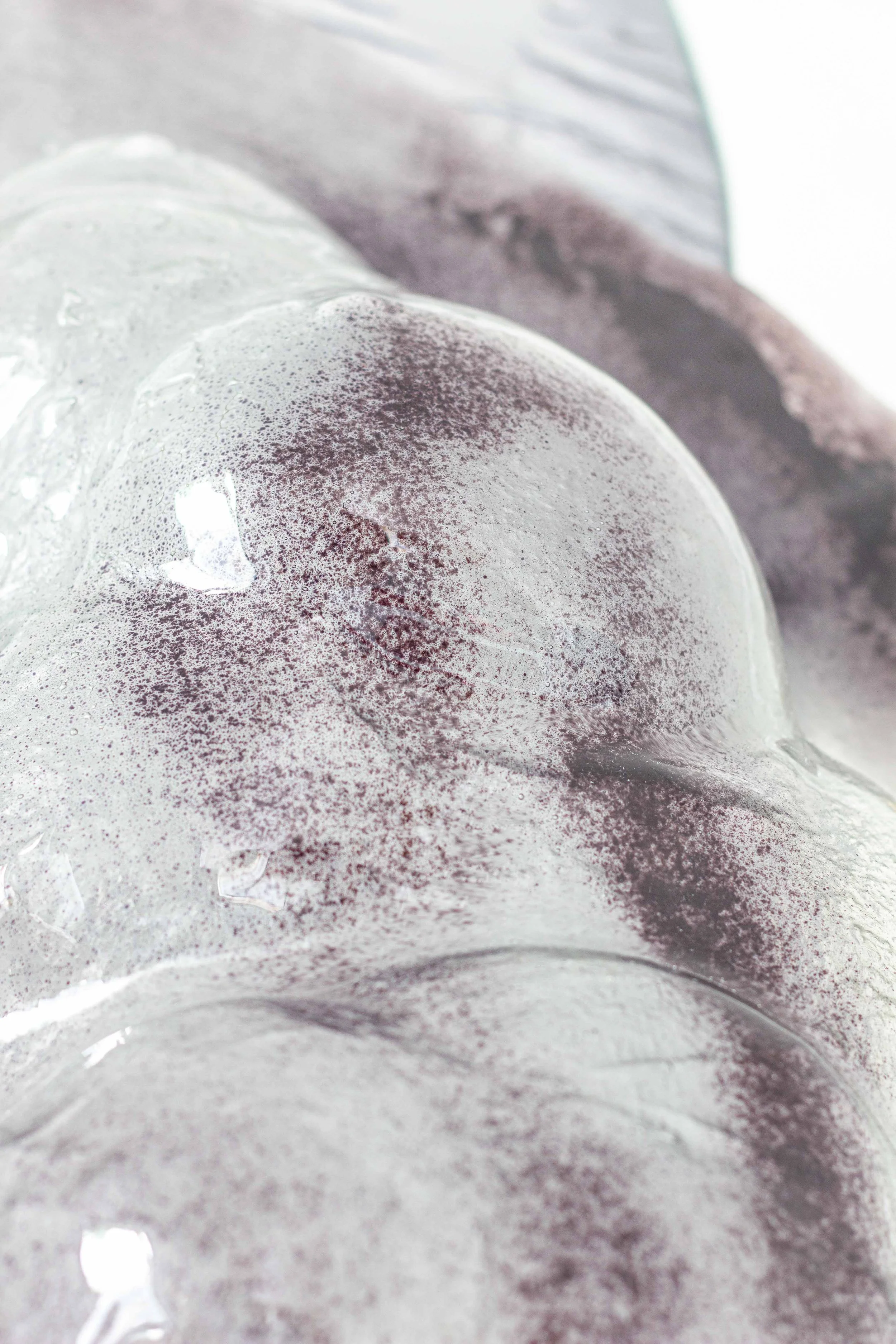 Una pietra di ghiaccio con una superficie liscia e traslucida, leggermente appiccicosa, con alcune sfumature di colore viola e rosa.