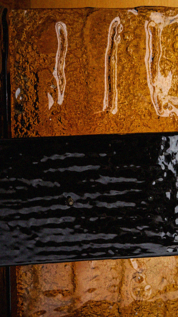 Dettaglio di una pietra di mosaico con un motivo che ricorda le onde del mare, con un'area nera con un effetto ondulato e riflettente sopra di essa.