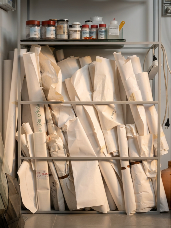 Scaffale con vari rotoli di carta o tessuto avvolti, sopra bottiglie di medicinali o sostanze chimiche in contenitori di plastica, in un ambiente di laboratorio o studio.