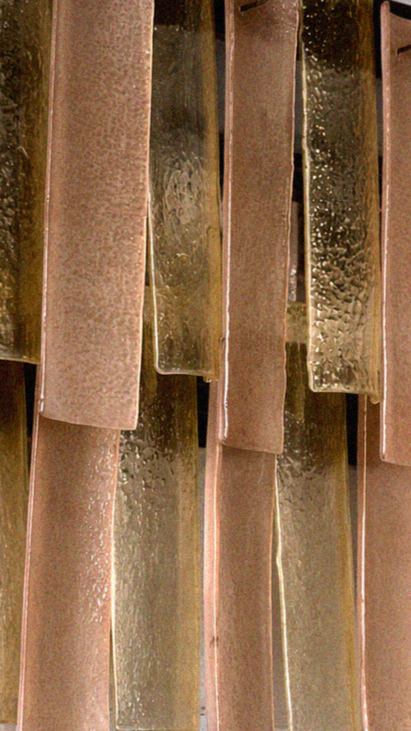 Sei pezzi di vetro colorato, appesi in modo verticale, con superfici texture e riflessi di luce.
