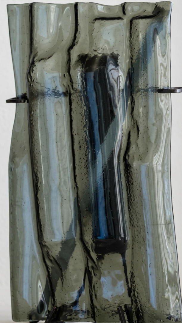 Un'opera d'arte astratta realizzata con vernice su una grande superficie di plastica o vetro, con colori nero, blu, bianco e beige che si combinano in motivi fluidi e astratti.