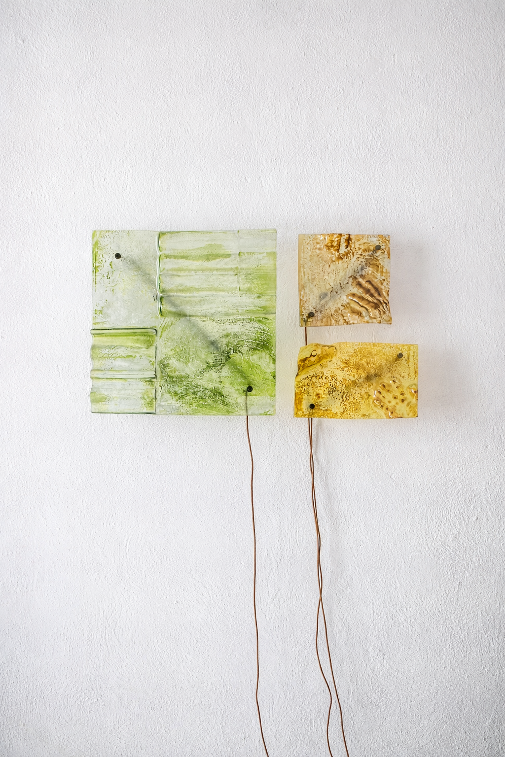 Due pannelli di arte astratta appesi a una parete bianca, uno verde e uno giallo, collegati da fili sottili.