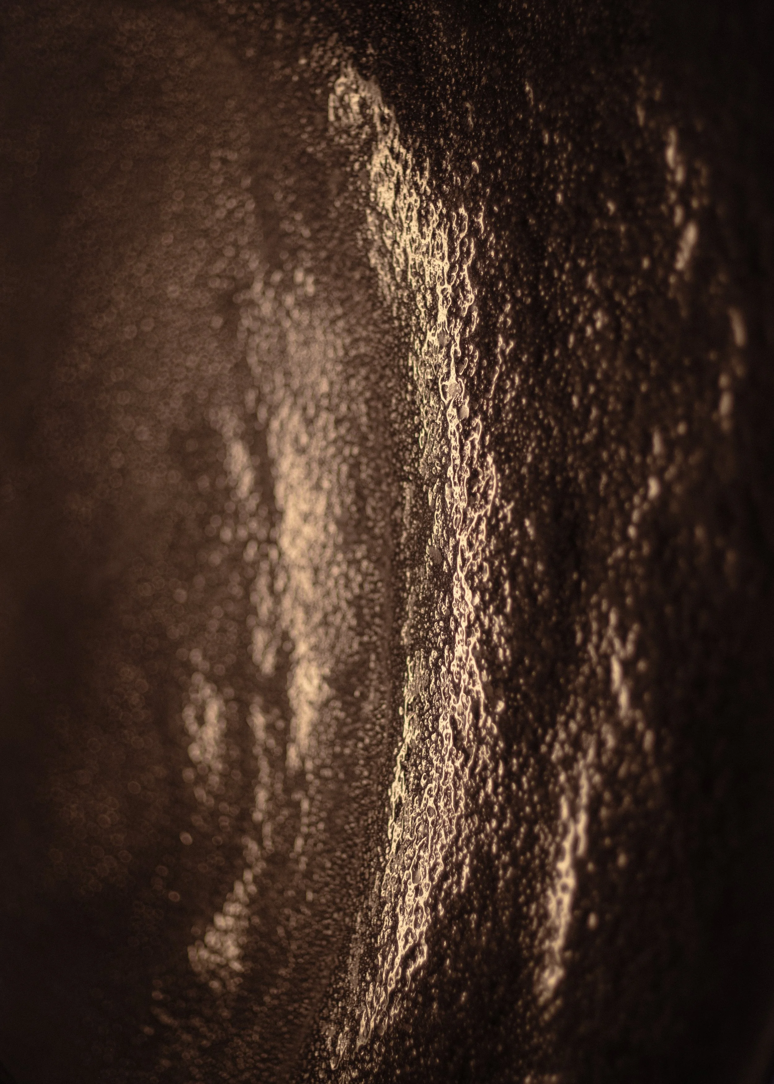 Close-up di gocce di condensa o brina su una superficie nera, con riflessi di luce dorata