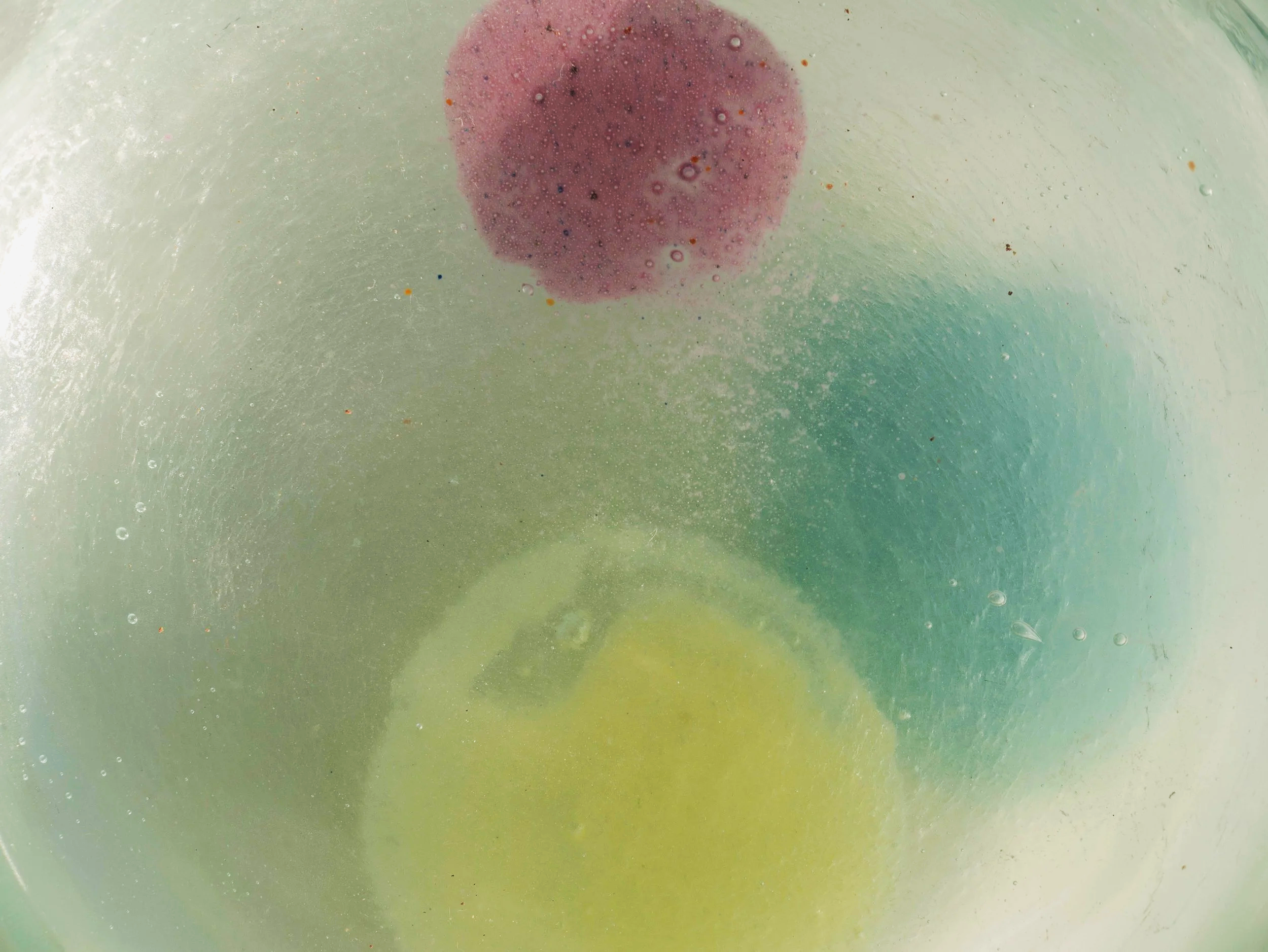Un liquido color verde con una macchia rossa centrale e piccole bolle d'aria sulla superficie.