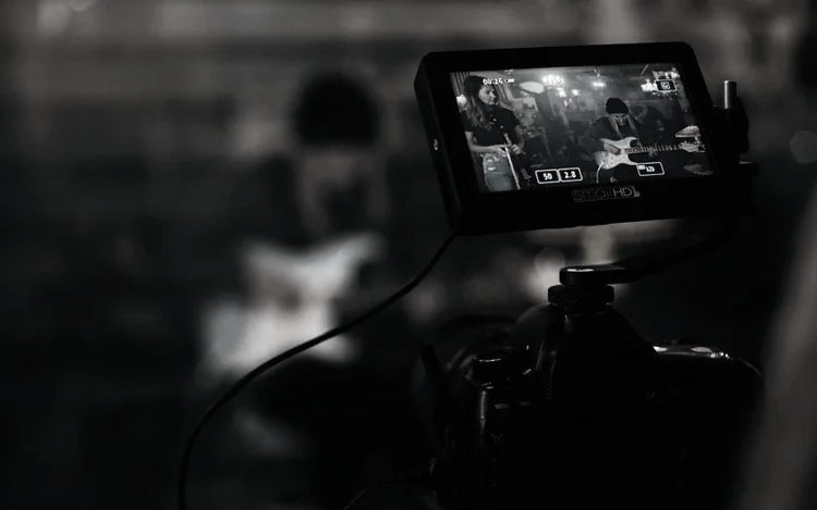 A digital camera recording a live music performance with two musicians playing guitars in a dimly lit setting.