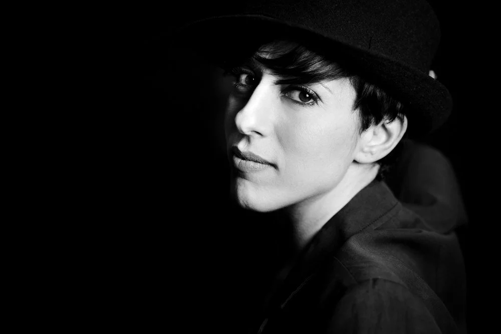 Black and white portrait of a woman with short hair, wearing a hat, looking directly at the camera with a serious expression.
