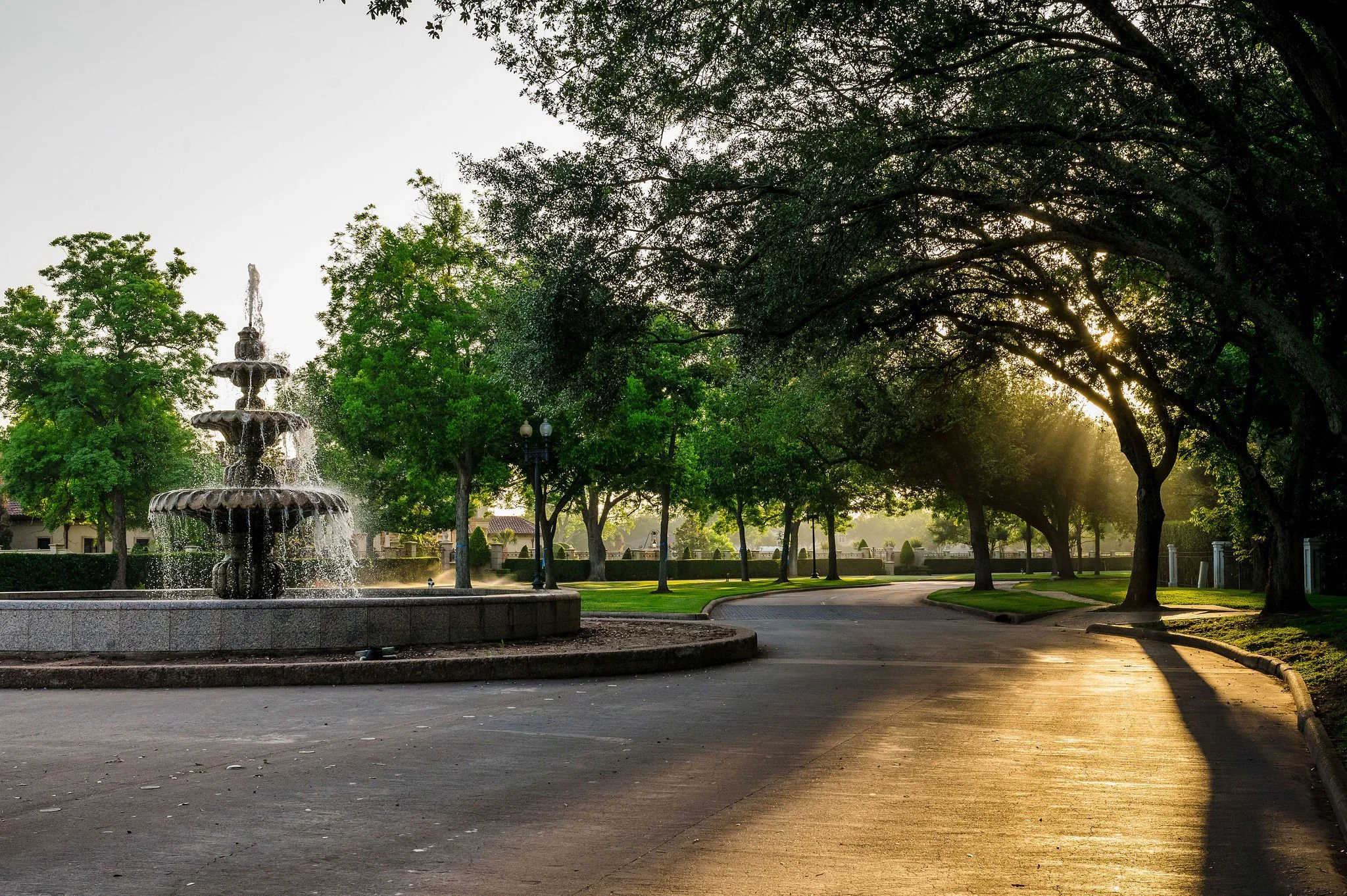 Sunrise illuminating a fountain and tree-lined Sugar Land street