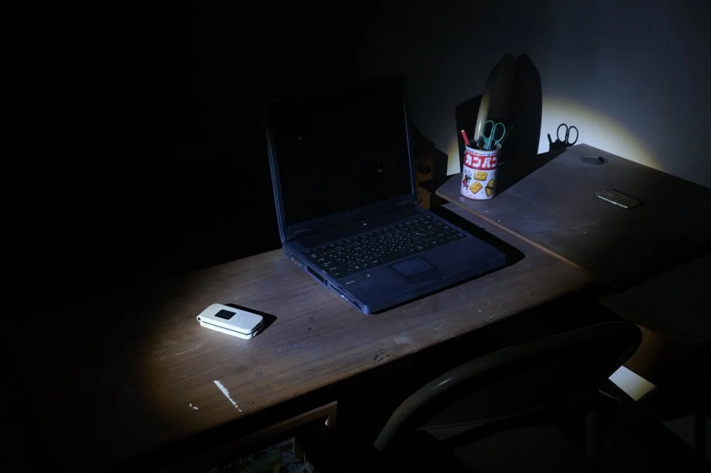 Installation view of Ghosts of Tomorrow at Gallery ETHER, with a laptop and objects from the Kinugawa Onsen project illuminated by flashlight.