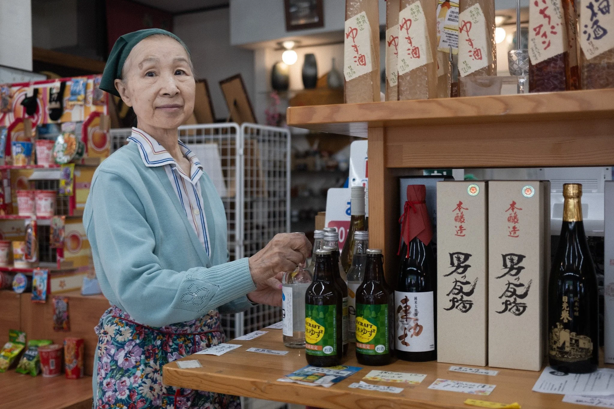 Owner of souvenir shop Kodaka, Kinugawa Onsen, standing beside bottles and local products.