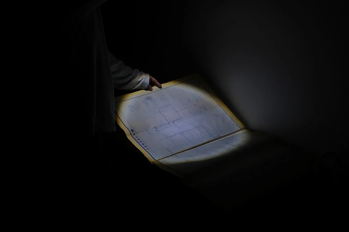 Visitor examining the old blueprint of a now-abandoned hotel using a flashlight inside the Ghosts of Tomorrow installation.