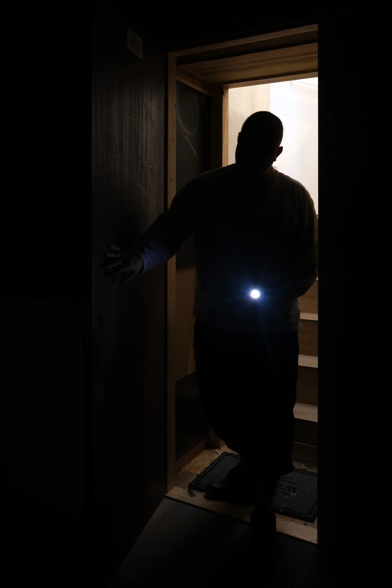 Silhouetted visitor opening the door into Ghosts of Tomorrow, an installation on Kinugawa Onsen at Gallery ETHER, guided by a flashlight.