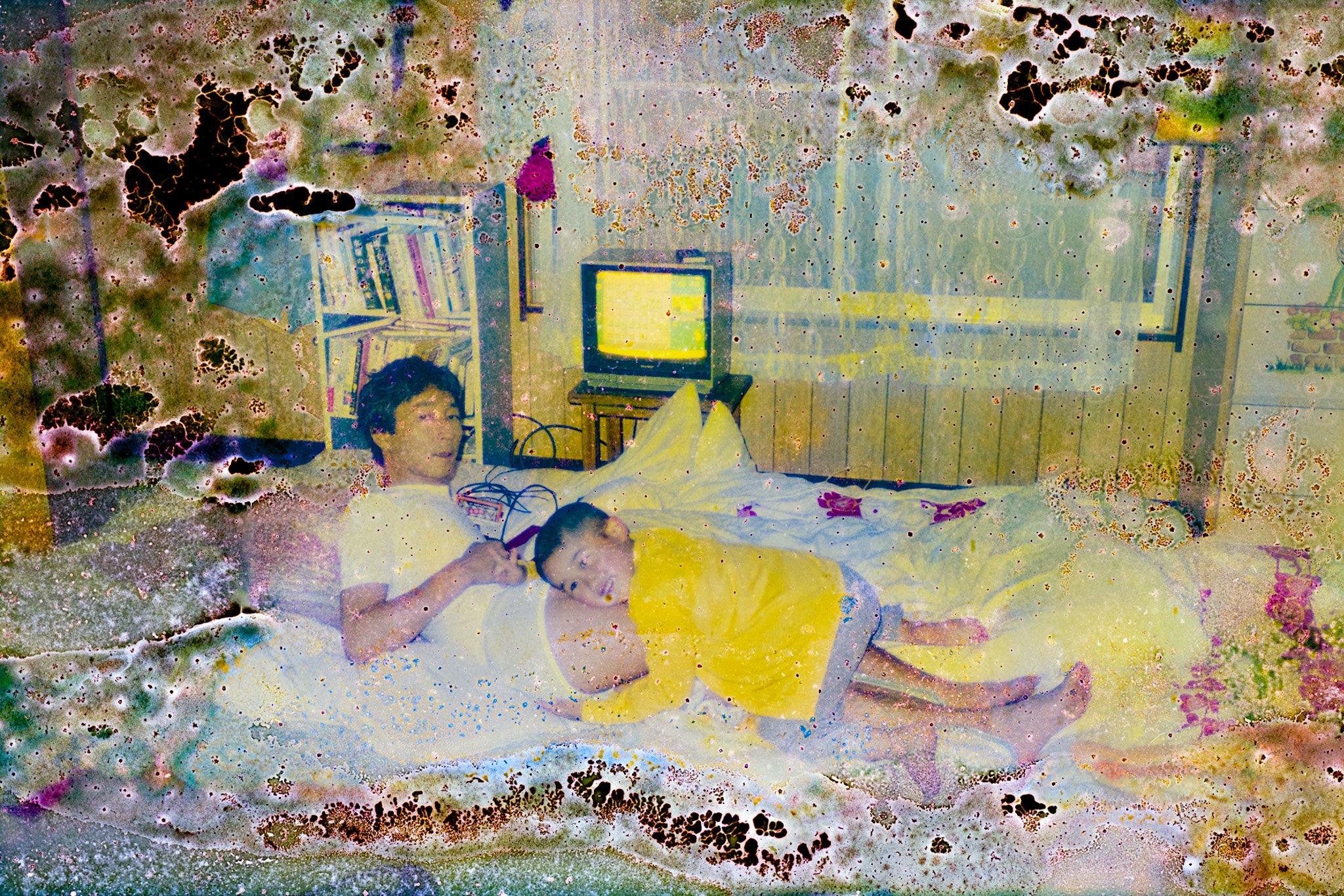 Damaged found photograph of a man and child, probably his son, playing FAMICON videogames on a bed