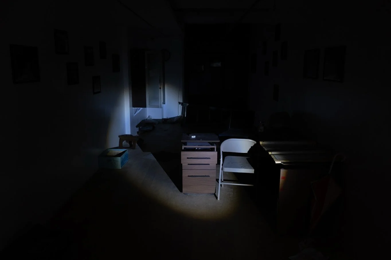 Abandoned-looking room with desks and chairs, partially illuminated by flashlight in the "Ghosts of Tomorrow" installation at Gallery Ether.