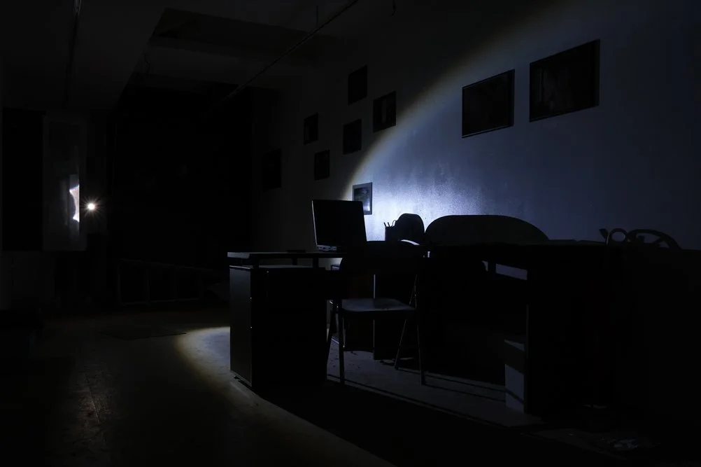 Dark room in the Ghosts of Tomorrow installation, with desks, chairs and photographs relating to Kinugawa Onsen.