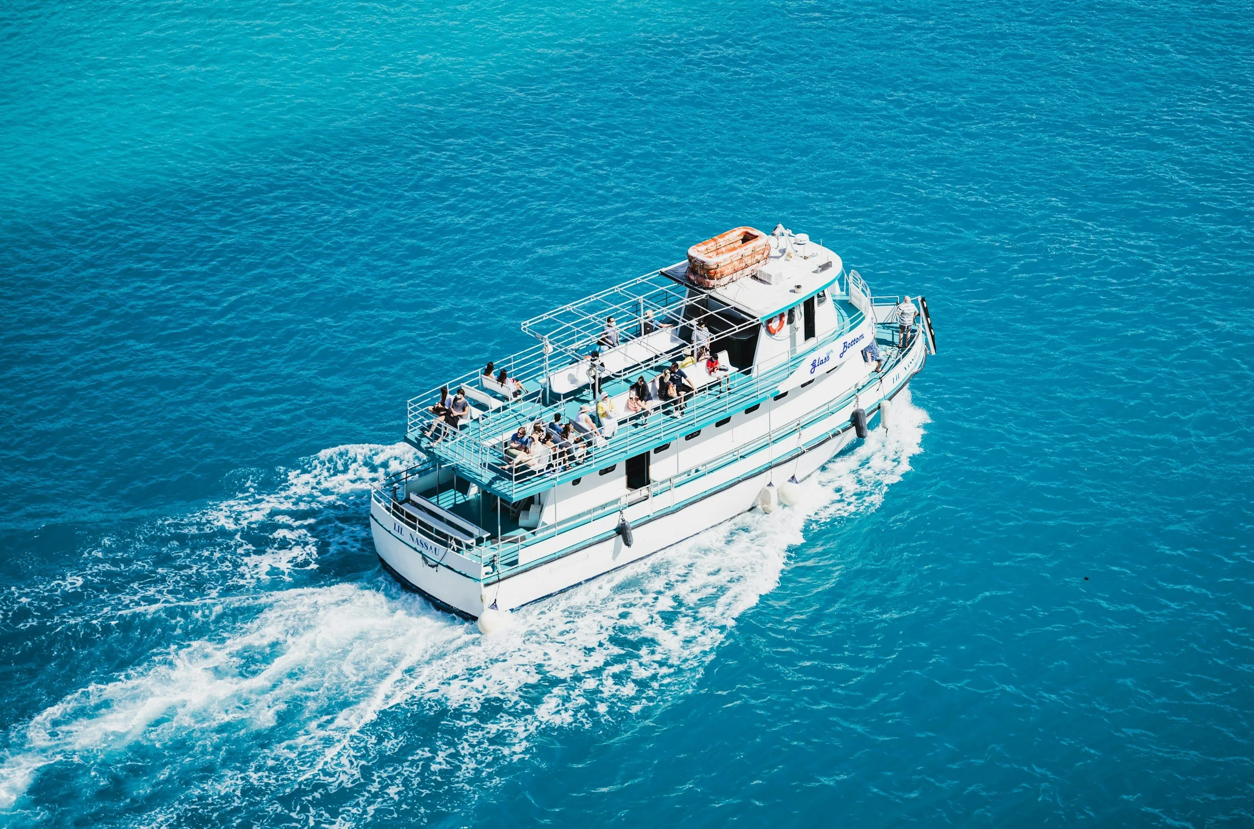 A white boat named Lil Nassau sailing on blue ocean water, with passengers on deck enjoying the ride.