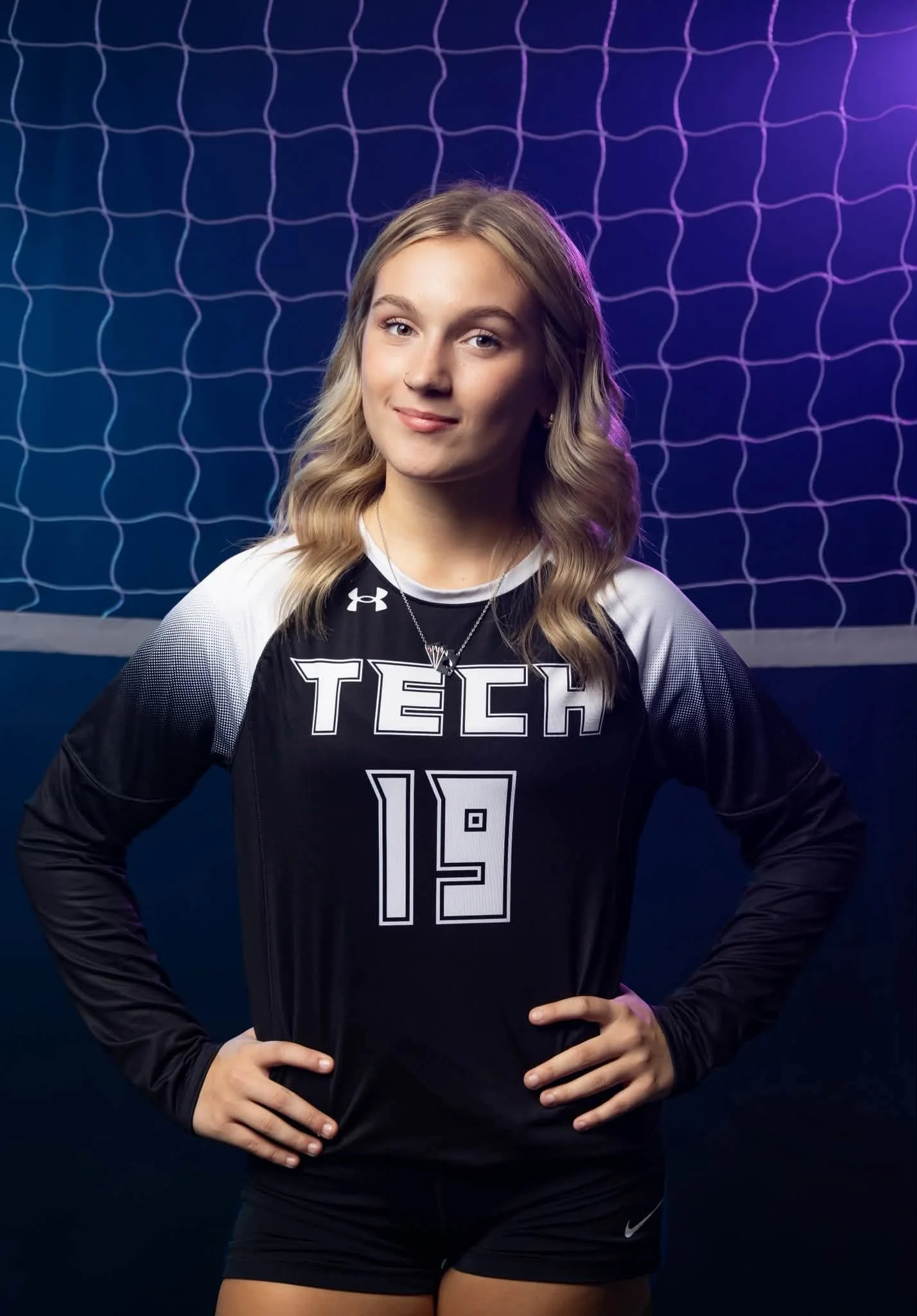 A young woman with blonde wavy hair wearing a black and white athletic jersey with the number 19 and the word 'TECH' printed on it, standing with her hands on her hips in front of a blue background with a volleyball net pattern and purple and blue li