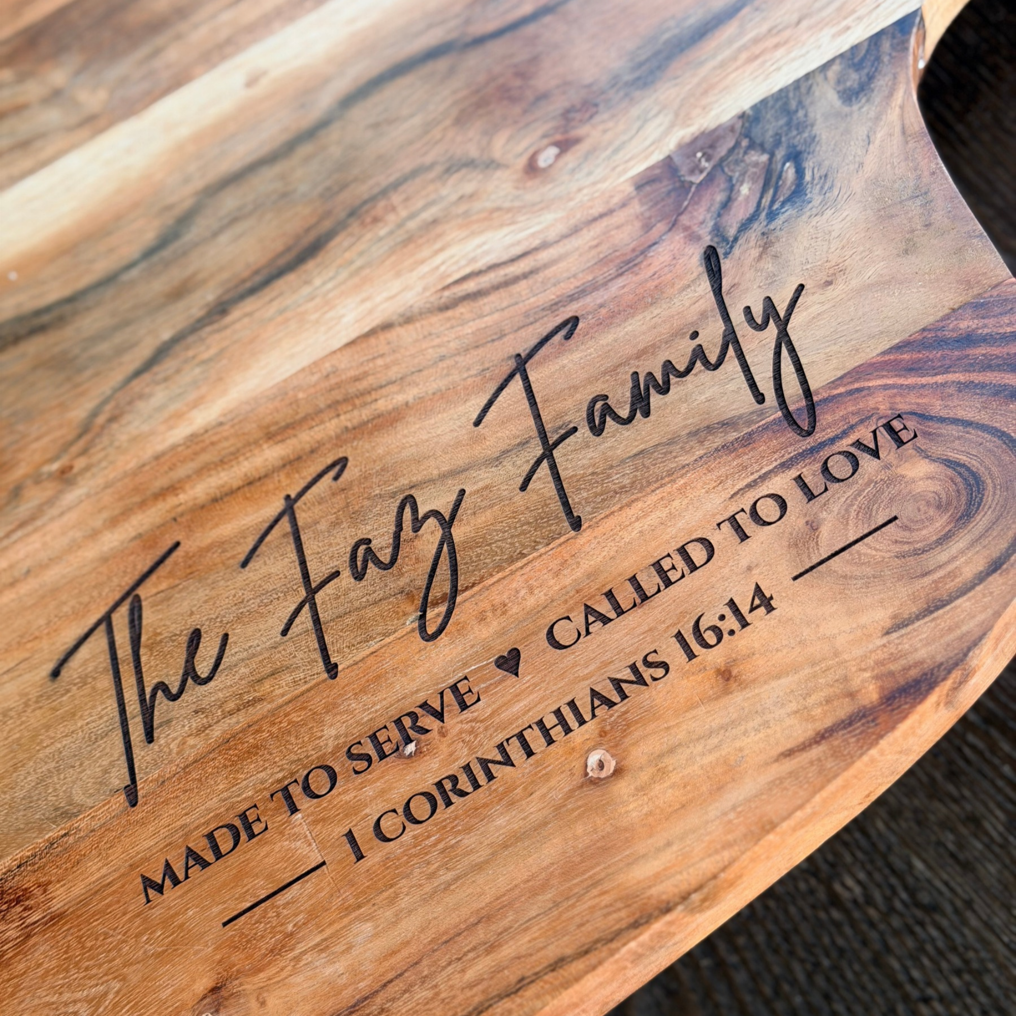 Close-up image of a wooden plaque with black cursive text engraved on it, partially visible, with a textured, dark background.