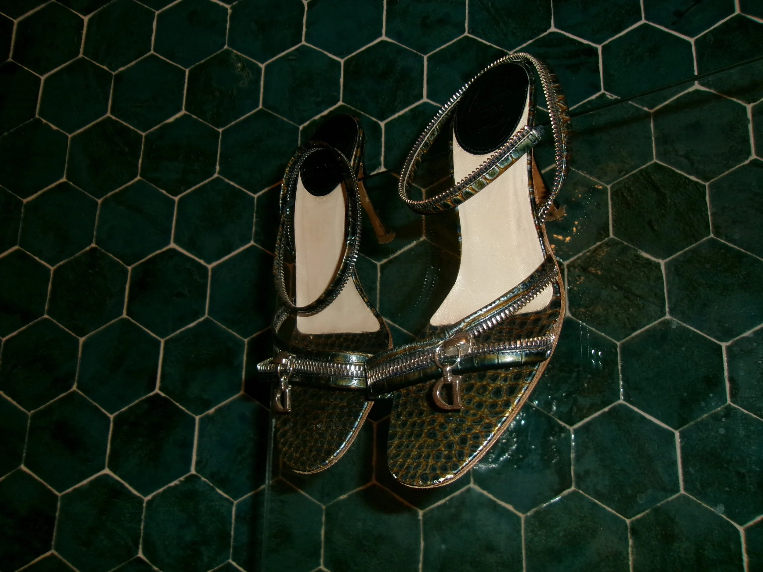Pair of high-heeled shoes with a textured, snake-skin pattern, placed on a dark green tiled floor.