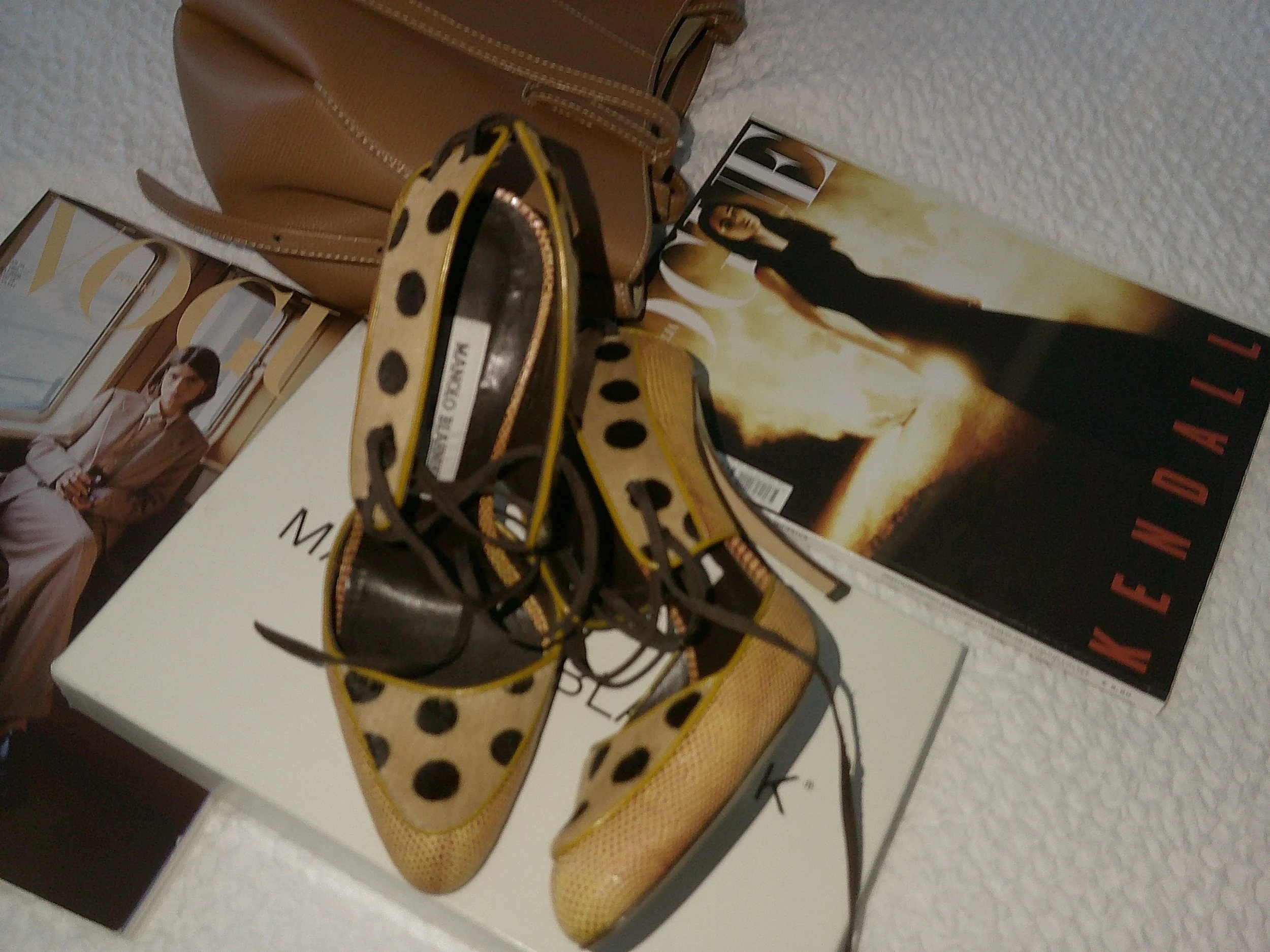 A pair of yellow and black polka dot sneakers resting on top of magazines, including a fashion magazine featuring a woman in a beige blazer and another magazine showing a woman in a long black dress.