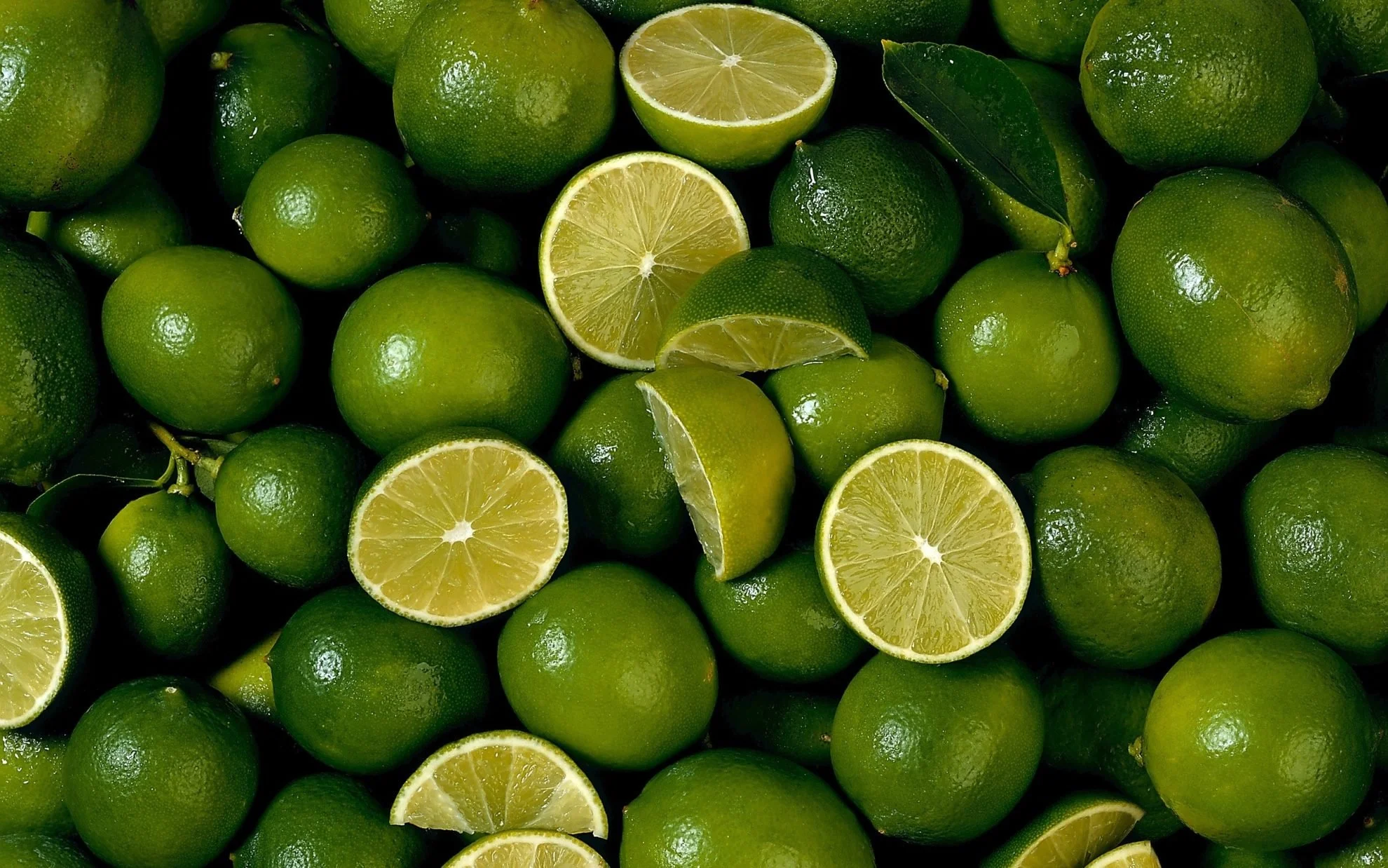 A pile of fresh green limes, some cut in half showing the juicy interior.