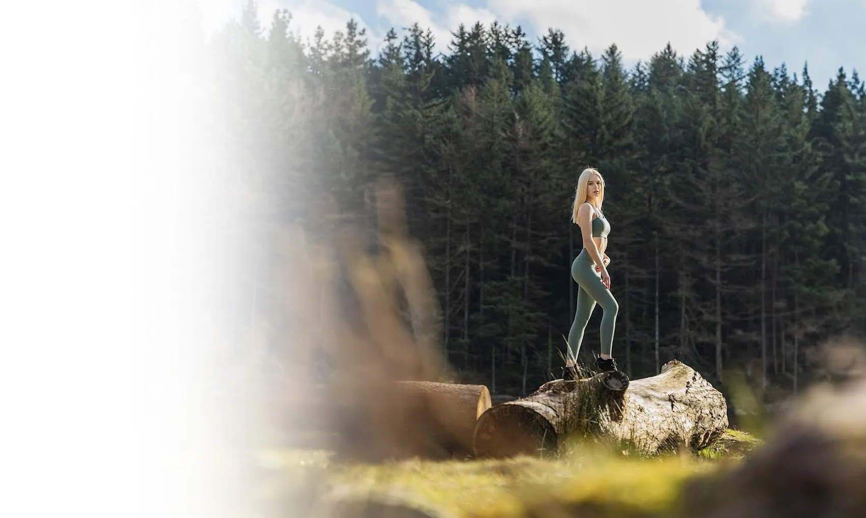 A woman in athleticwear standing on a fallen tree trunk in a forested area during daytime.