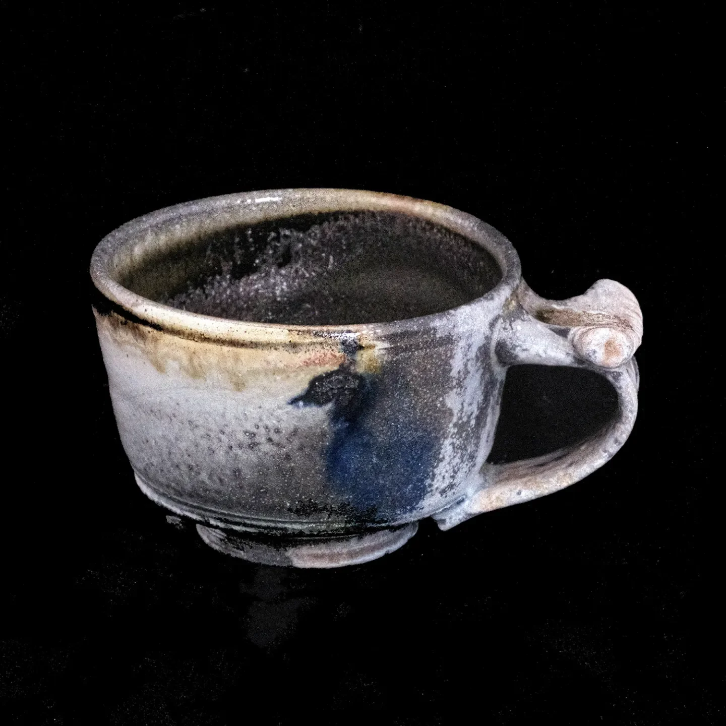 A ceramic cup with a handle, decorated with a sumi-e design, set against a black background.