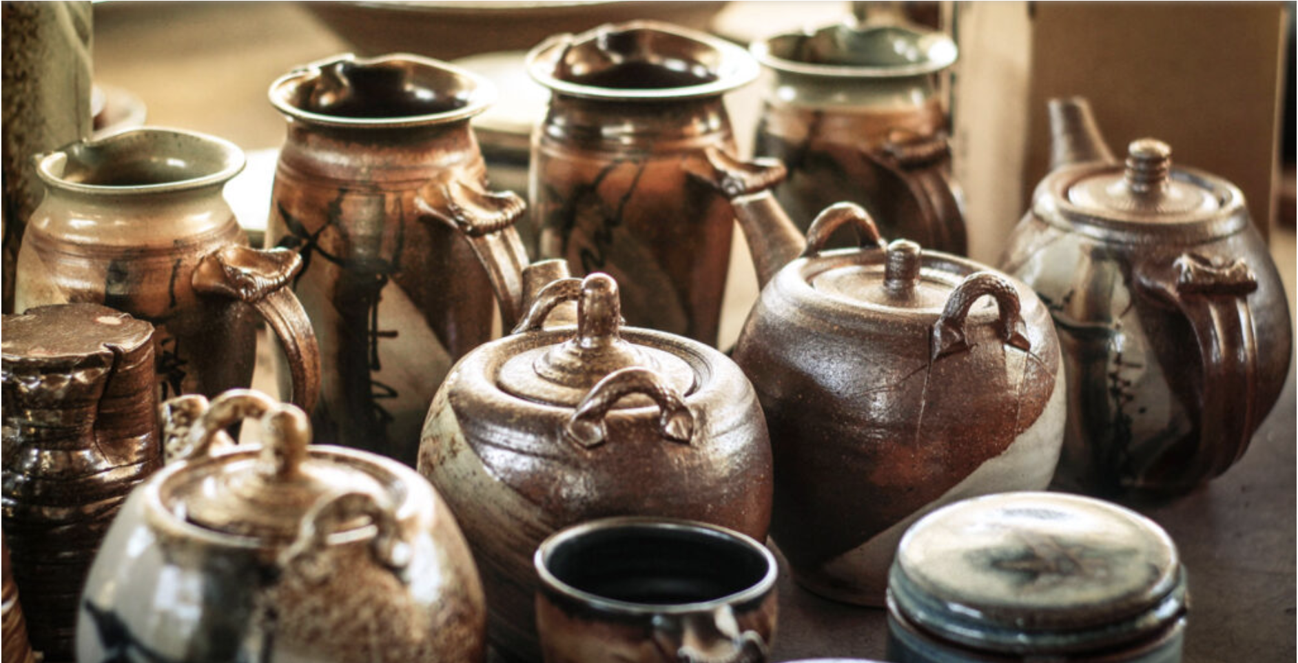 Collection of brown ceramic pots and jars with lids, some with handles, on a wooden surface.