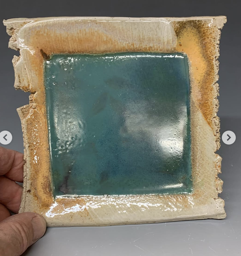 A square glass piece with a textured border, featuring a blue-green glazed center with iridescent and mottled effects.