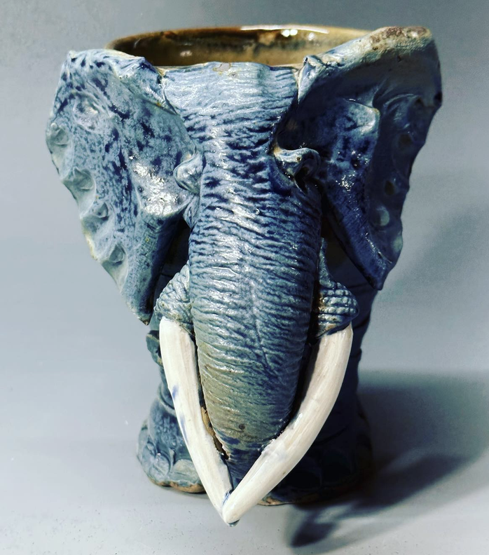 Ceramic mug designed to look like an elephant's face, with detailed ears, trunk, and tusks.