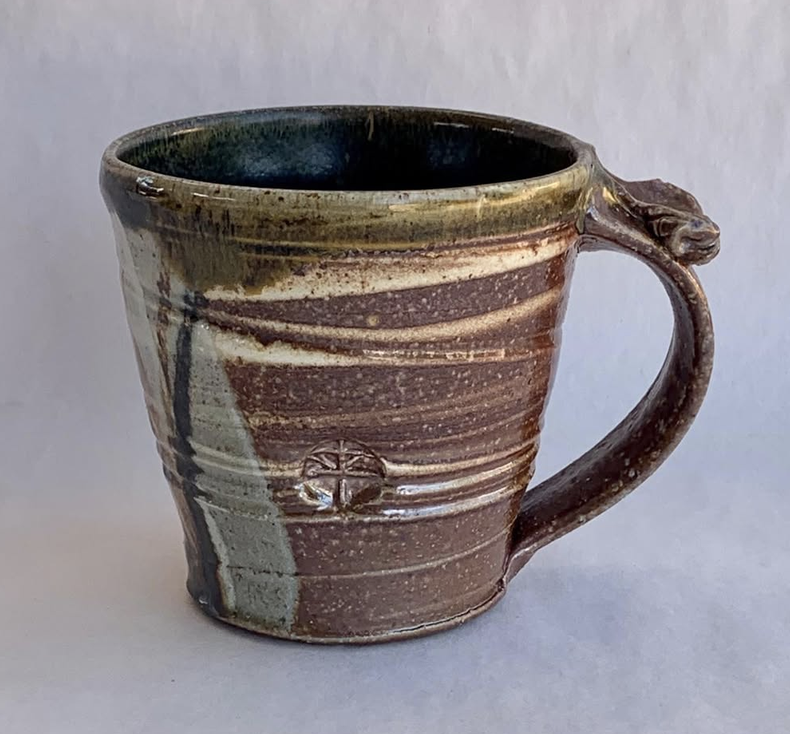 Ceramic mug with a brown and beige striped glaze and a small face-shaped handle, set against a plain background.