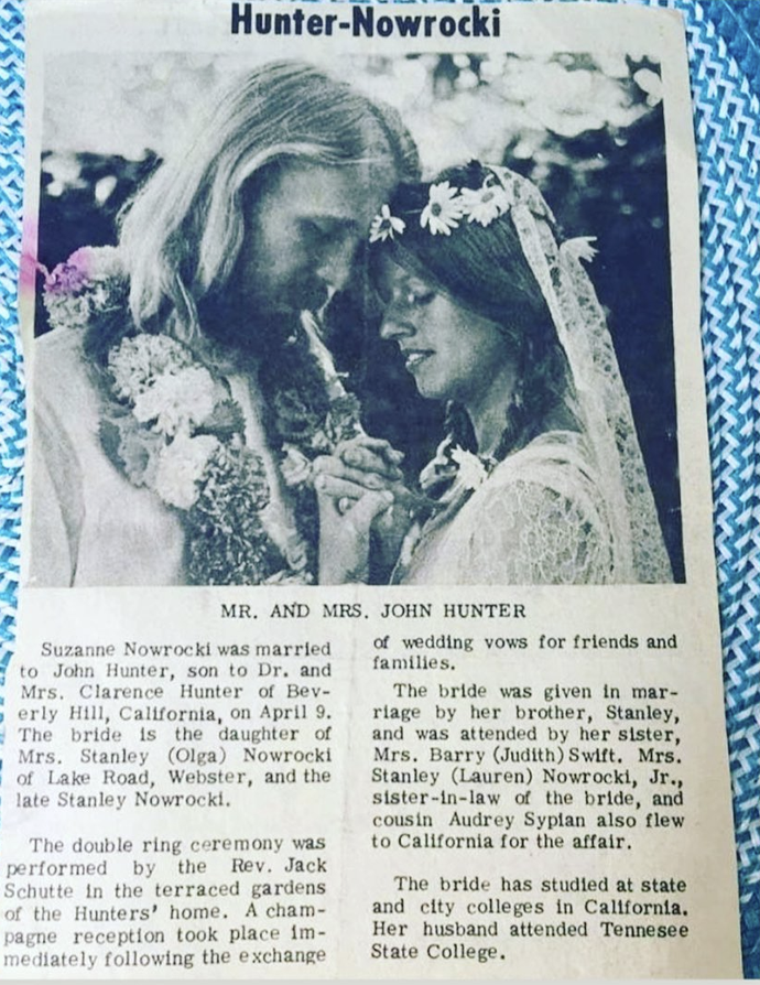 Black and white wedding announcement photo of Mr. and Mrs. John Hunter, with the bride wearing a lace gown and floral headpiece, and the groom with long hair, embracing with foreheads touching.