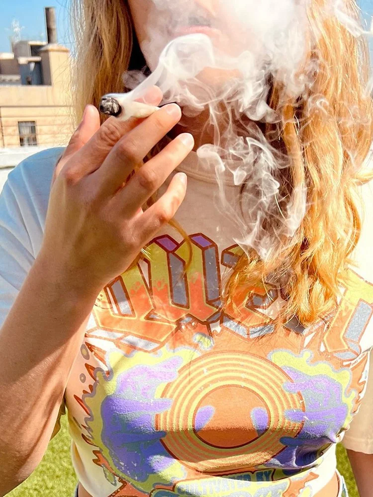 Person smoking with colorful shirt and smoke rising outdoors