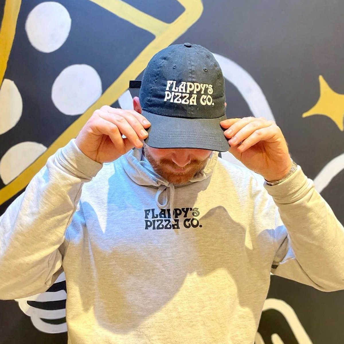 Person wearing a cap and hoodie with Flappy's Pizza Co. logo