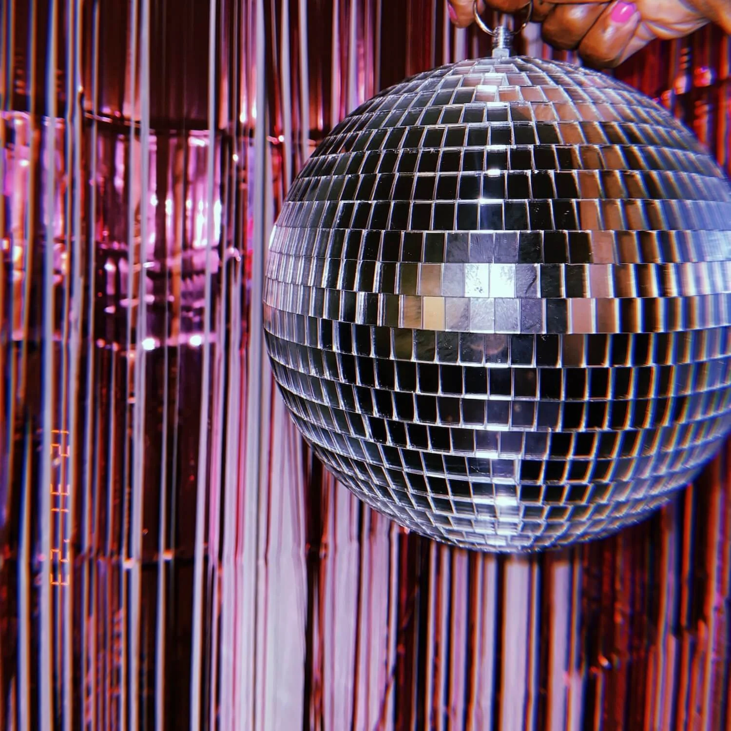A mirrored disco ball hanging in front of multicolored vertical strings or ribbons.