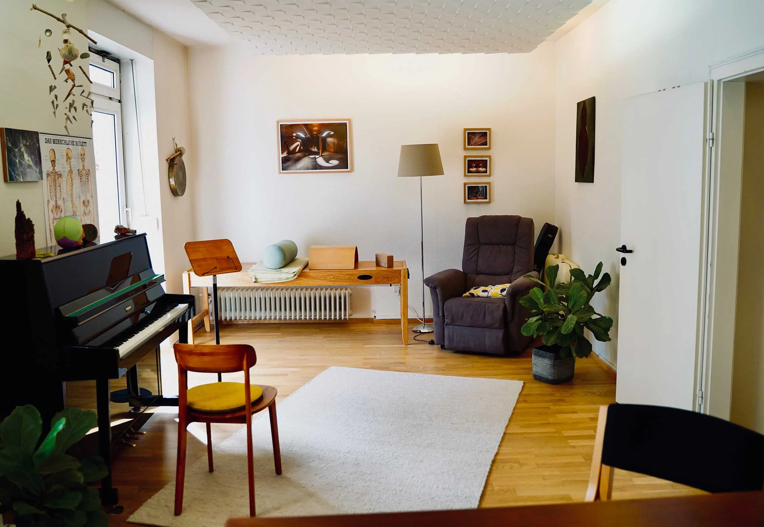 Behandlungsraum für Stimmtherapie in Köln-Ehrenfeld mit Klavier, Notenständer, Therapieliege und Sessel