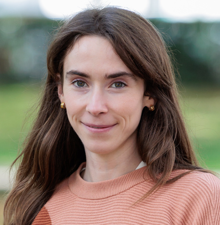 Close-up of Emma Antonio, a smiling woman with brown hair, wearing a pink sweater and gold earrings outdoors. Emma Antonio is a battery researcher at Imperial College London working in high-performance sodium ion batteries.