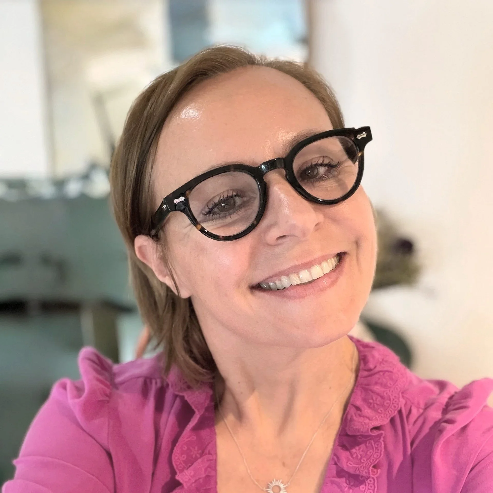 Magda Titirici, a woman smiling with shoulder-length brown hair, wearing black round glasses, a magenta top, and a daisy-shaped necklace, in an indoor setting. Magda Titirici is a professor at Imperial College London leading in high-performan